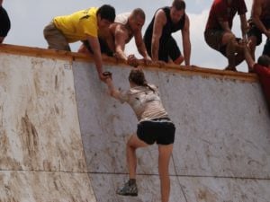 Group of People Helping Woman Finish Climb Up a Wall