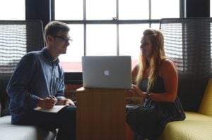 Man and Woman Talking in Front of a Mac Laptop